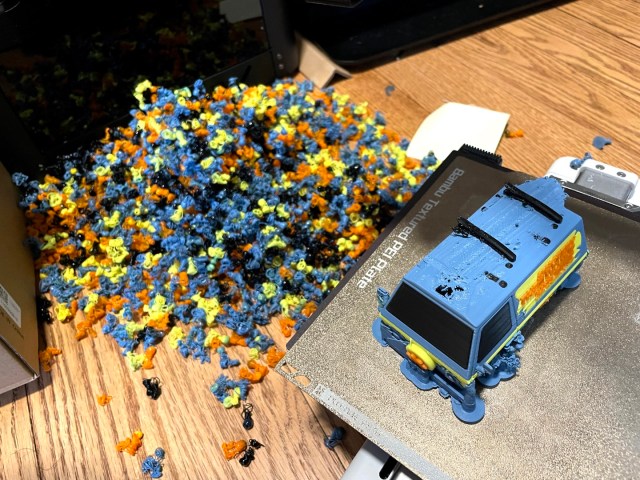 A 3D printed model of the Mystery Machine van in the foreground, and a pile of waste plastic bigger than the van in the background.